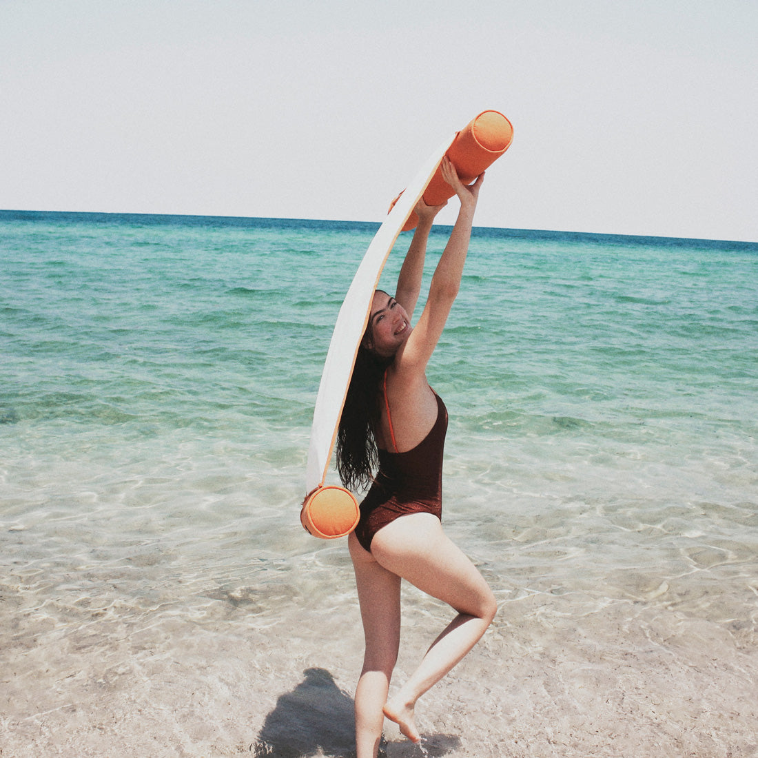 A women on a beach dragging a luxury pool float in the wind.