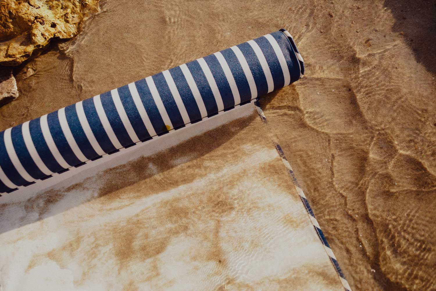 A beach float for adults lying on the beach with water and sand flowing over the float.