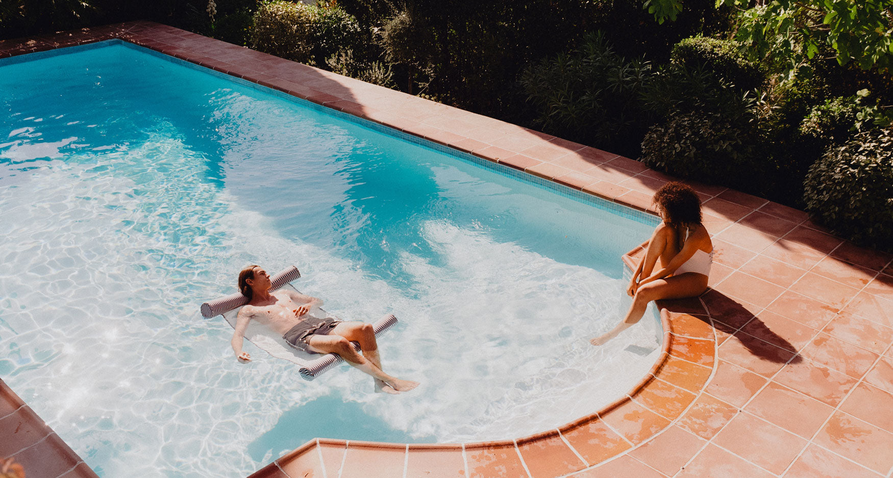 A women sitting by a pool with a man on a luxury pool float hammock