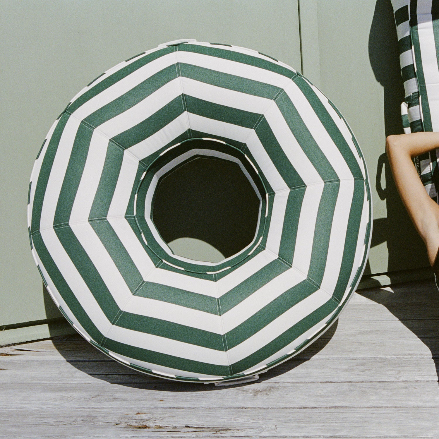 A green and white striped fabric ring pool float lounger for adults leaning against a pool house.