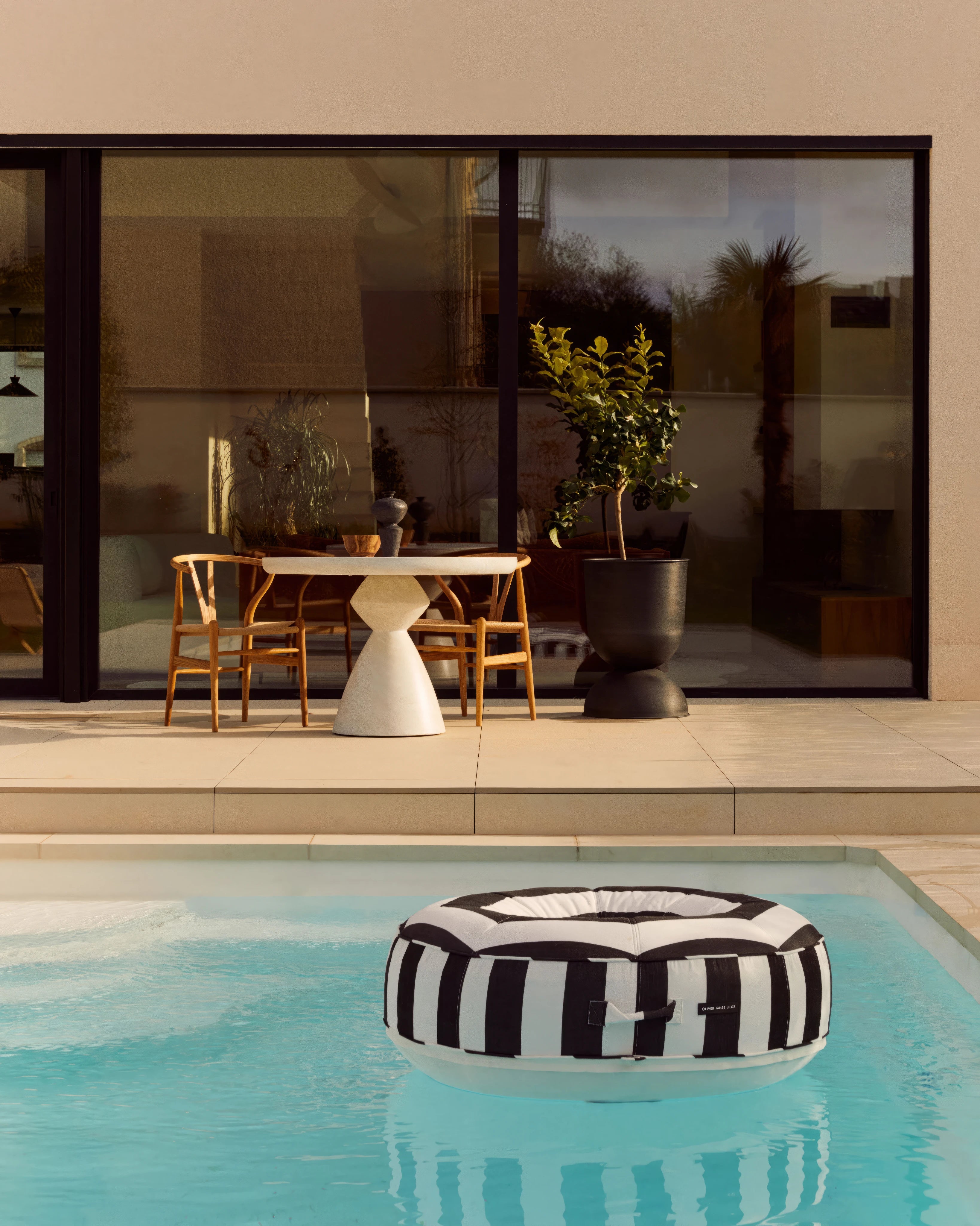 A sculptural ring float in bold black-and-white stripes floats in a minimalist pool beside a contemporary terrace — a seamless blend of form, function, and refined leisure.