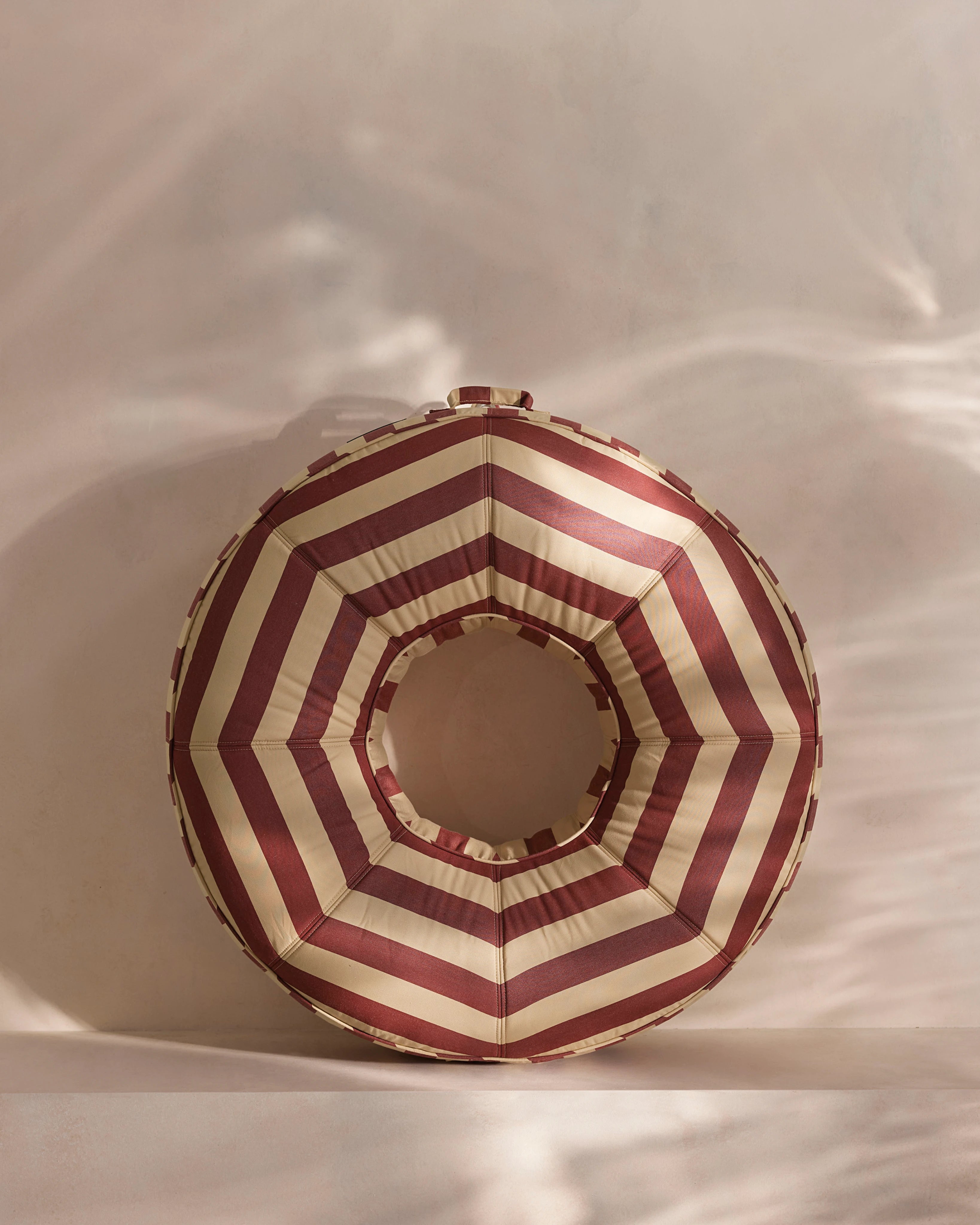 Round luxury pool float with bold red and beige chevron stripes, designed for adults — a high-end pool accessory from Oliver James Lilos for elegant relaxation.