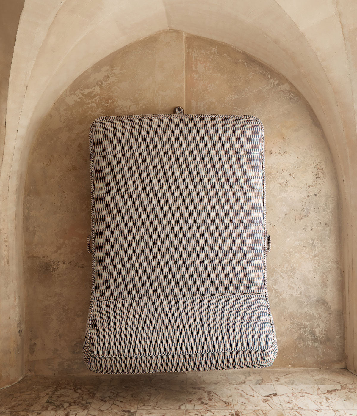 A luxury pool float hanging beneath a marble stone archway by an eyelet using a hook made of teak and stainless steel hook.