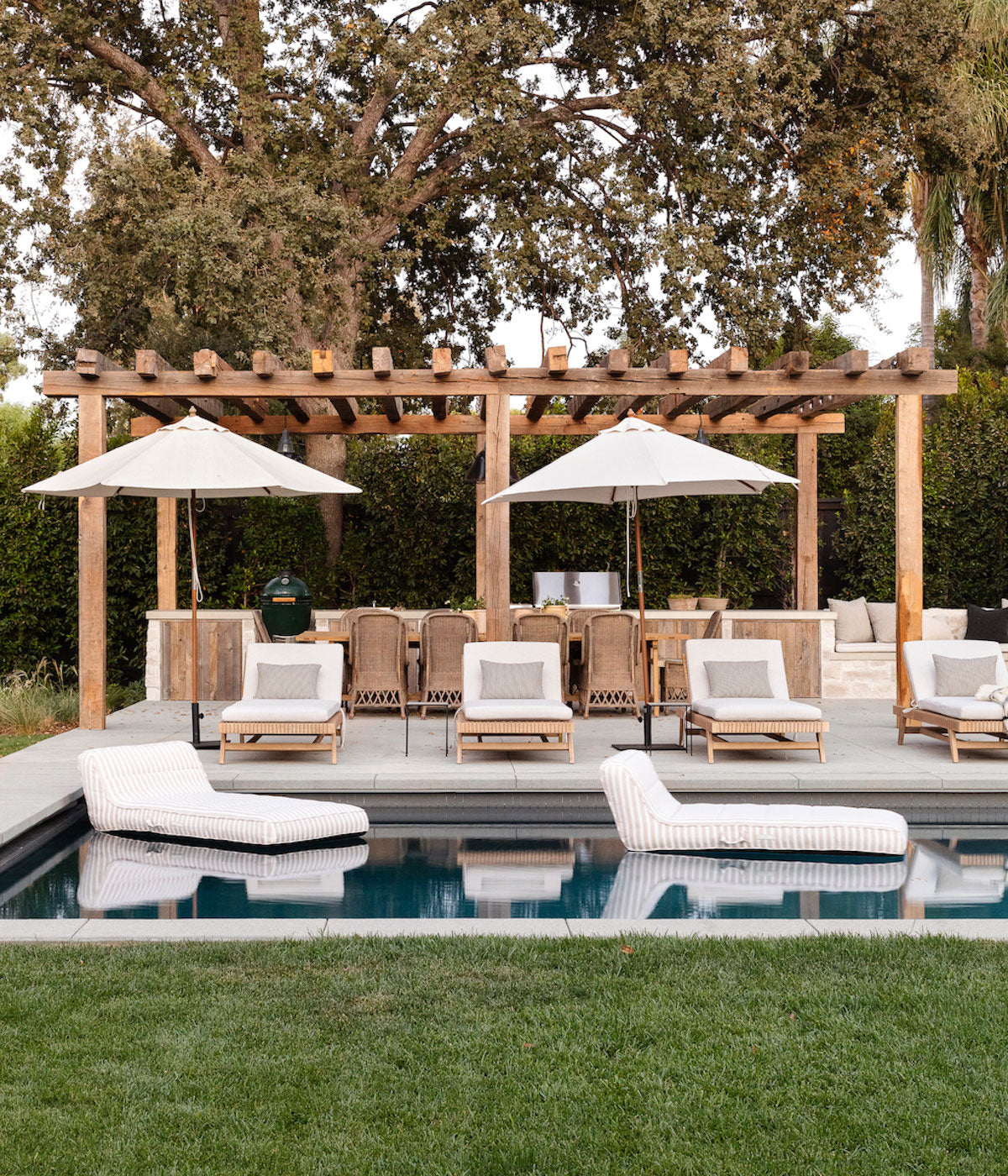 Two pool floats for adults floating in a swimming pool inside an interior designer's garden with matching parasols and outdoor furniture.