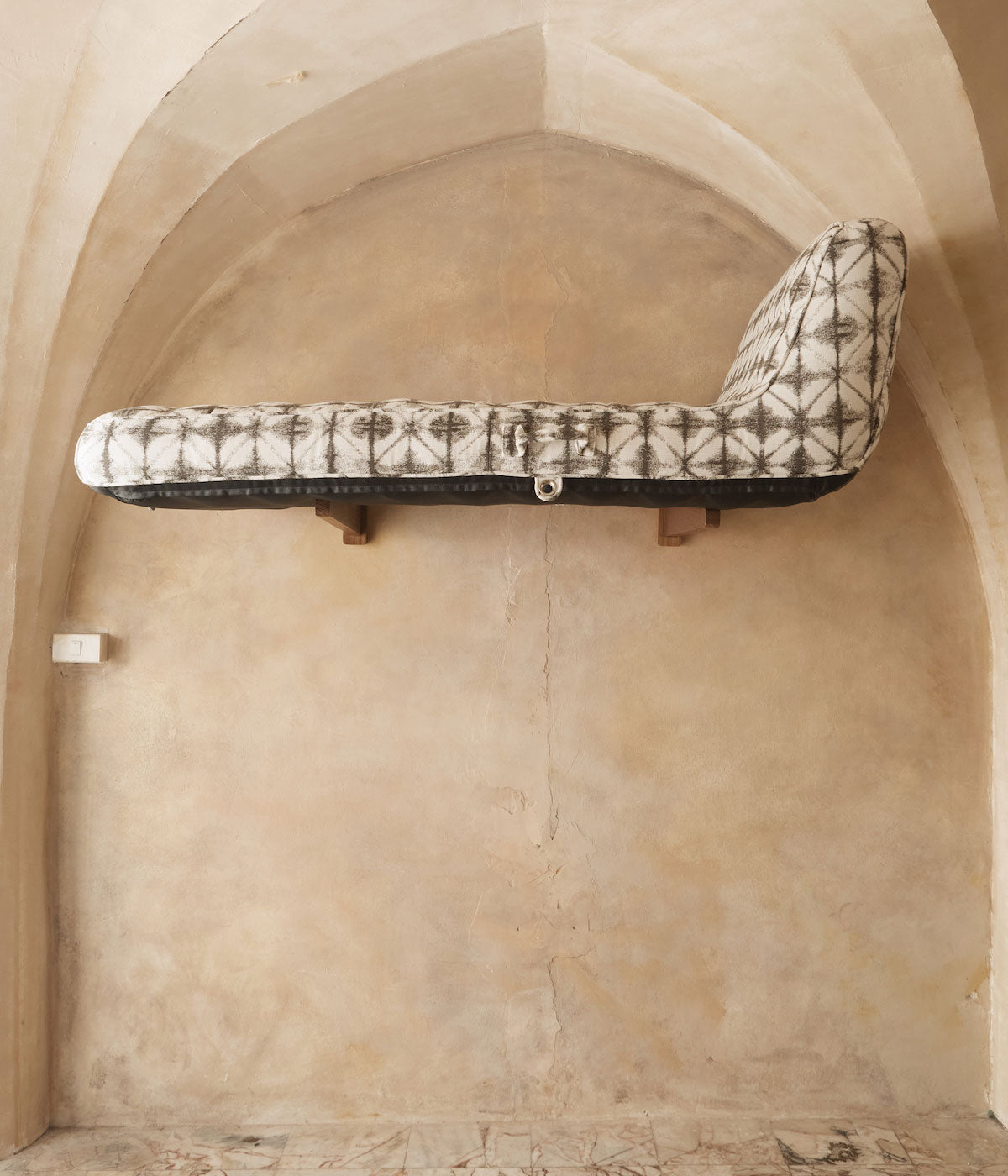 A pool float for adults sitting on surf rack made of teak beneath a marble stone archway.